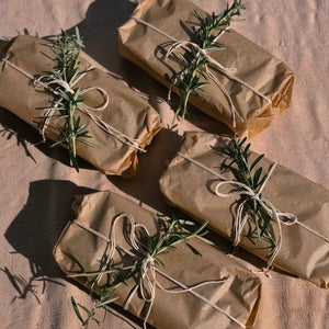 Four packages of food wrapped in the If You Care Unbleached Waxed Paper with string and rosemary on a textured surface.