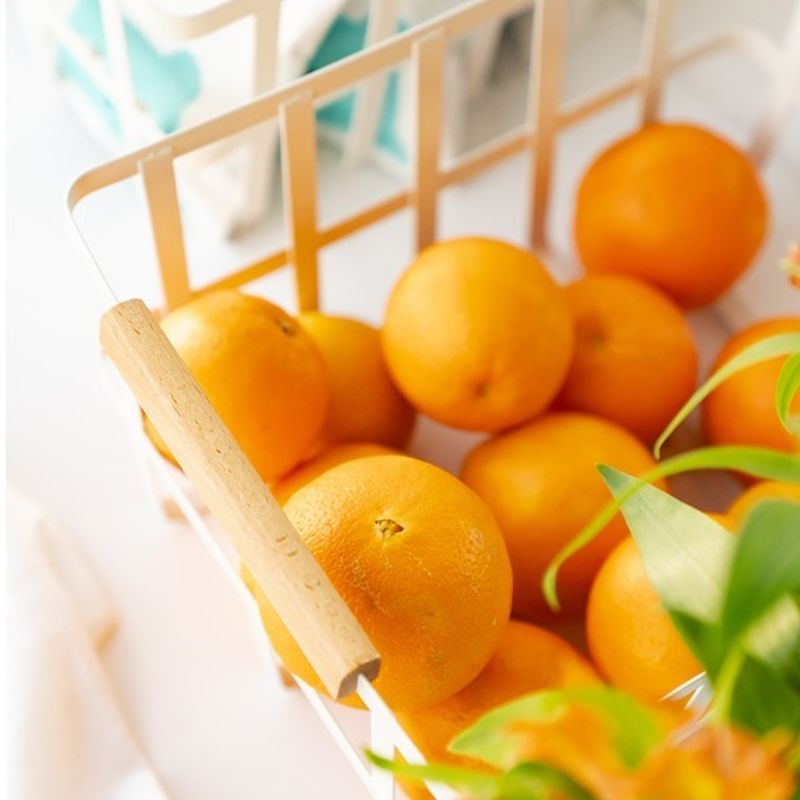 Close-up of wooden handle on white metal basket; oranges inside the basket.
