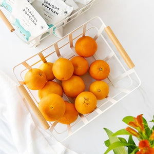 Top-down view of white metal basket with wooden handles filled with oranges.