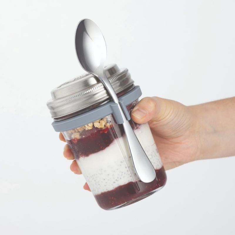 Person holding a filled Kilner Breakfast Jar with spoon secured in the silicone band.