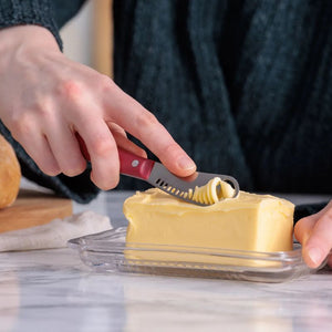 Person using a butter curling knife to remove butter from a block.