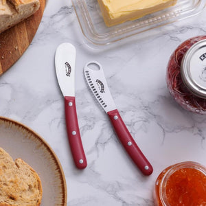Two Kilner Butter Spreader & Knifes with red handles on a marble surface next to bread and jam.