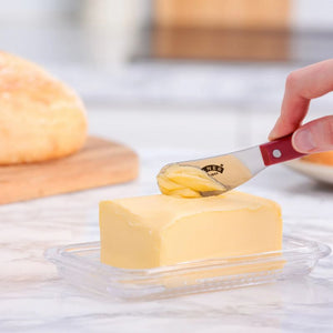 Kilner butter spreader being used to remove butter from a block with a loaf of bread in the background.