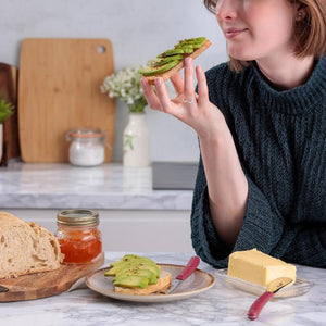 Person holding a slice of avocado toast in a kitchen setting with the Kilner butter spreader and tooling knife on the table.