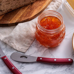 Jar of jam and the Kilner butter spreader and tooling knife nearby on a marble surface.