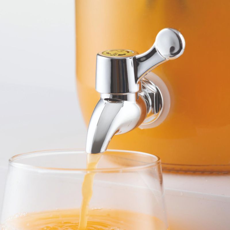 Tap on drinks dispenser shown open with orange juice filling a glass
