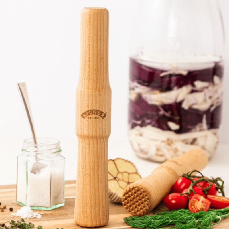 Kilner Fermentation Packer placed upright on a kitchen bench beside jars, vegetables, and a chopping board.