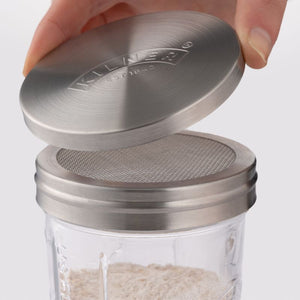 Hand lifting stainless steel lid from sifter attachment on Kilner glass jar.