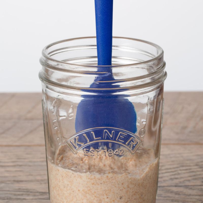 Kilner wide mouth glass jar with sourdough starter inside being mixed with a blue spatula.