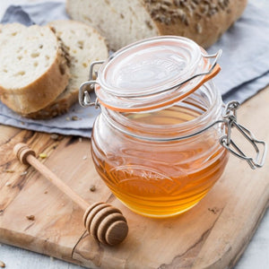 Wooden chopping board with filled Kilner beehvie-shaped honey jar, wooden drizzler and sliced bread