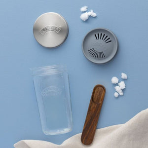 Kilner Kefir Set with a stainless steel lid, a gray strainer top, and a wooden spoon, arranged on a light blue background.