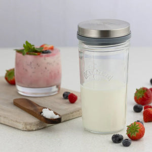 Clear glass jar with silver lid from the Kilner Kefir Se, on a white surface with berries and a pink smoothie.