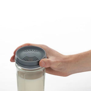 Hand holding a glass kilner jar with a gray lid on a white background