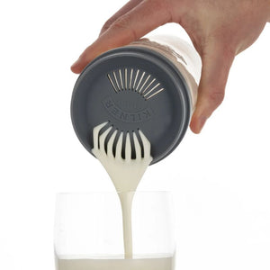 Hand holding the Kilner Kefir jar with a gray strainer lid pouring kefir milk, on a white background