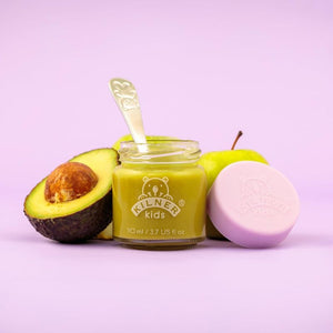 100mL Kilner Kids Jar filled with green baby food with a spoon, half an avocado, and a pink silicone lid on a light purple background.