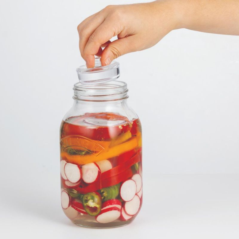Glass weight being lowered into a Kilner regular mouth jar to help keep vegetables submerged during a fermentation