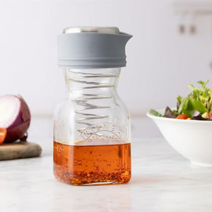 Kilner Salad Dressing Maker shown filled with salad dressing, styled next to salad and onions.