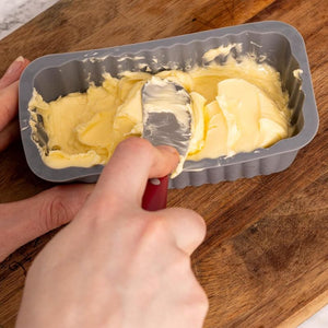 Hand using a spatula to press butter into the Kilner Silicone Butter Mould on a wooden surface