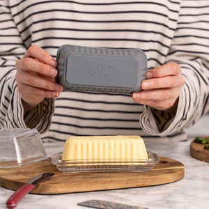 Person holding the Kilner Silicone Butter Mould over a butter dish on a wooden cutting board.