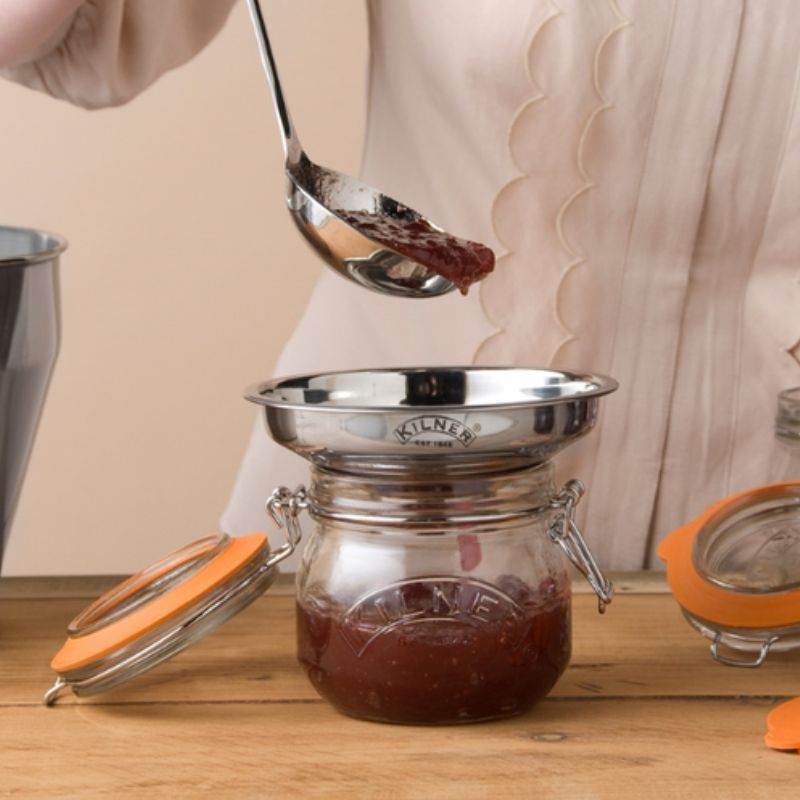 Person ladling homemade jam into a Kilner jar using stainless steel funnel