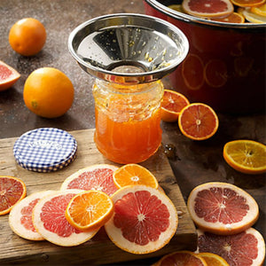 Kilner stainless steel funnel placed on a jar of orange marmalade with sliced citrus fruit on a wooden board.