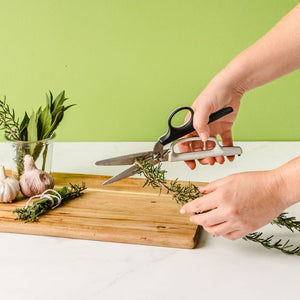 Dreamfarm Bishears kitchen scissors being used to cut fresh herbs on a wooden chopping board.