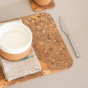 Rectangular cork placemat with white plate, napkin and cutlery.