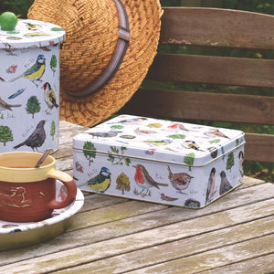 The Madeleine Floyd Bird Song Biscuit Tin with the matching biscuit barrel and tin tray - all styled on an outdoor dining table