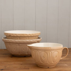 The Mason Cash Cane Batter Bowl styled next to two stacked mixing bowls, arranged on a wooden tabletop against a light grey panelled wall.
