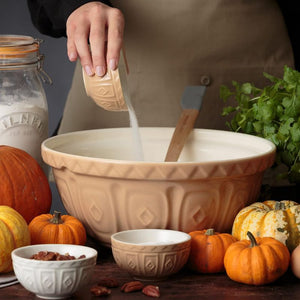 Person mixing in a large Mason Cash cane bowl surrounded by pumpkins and smaller the smaller cane prep bowls