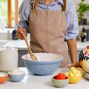 Person in a kitchen using the Mason Cash Home To Roost Hen Mixing Bowl in Blue, with various ingredients around.