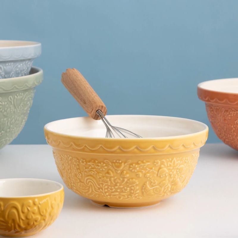 A round ceramic bowl with a warm yellow-gold finish, featuring embossed floral and hen patterns on the exterior and a smooth, slightly lighter interior, set against a plain white background.