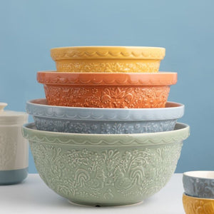 A stack of five nested ceramic mixing bowls with embossed floral and hen patterns by Mason Cash. Set against a solid light blue background.