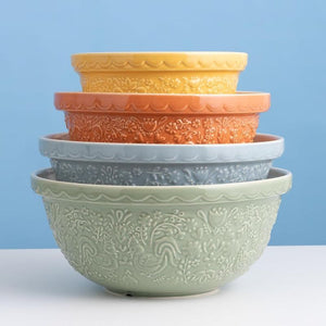 Five nested ceramic mixing bowls by Mason Cash with embossed floral patterns, stacked in a stack. The bowls are in pastel shades of sage green, light blue, orange, peach, and yellow, set against a solid light blue background on a white surface.