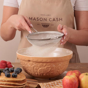 Person sifting flour into the Mason Cash In The Forest Bear Mixing Bowl in Cane with fruits on a table