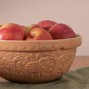 Mason Cash In The Forest Bear Mixing Bowl in Cane colour filled with red apples on a green surface.