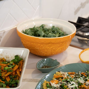 Mason Cash In The Forest Bear Mixing Bowl in Ochre, with green leafy vegetables and other ingredients on a kitchen counter.