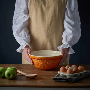 Person holding the Mason Cash In The Forest Bear Mixing Bowl in Ochre on a wooden table with apples and eggs.