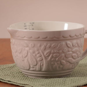 Close up of the Mason Cash In The Forest Fox Measuring Jug in Stone showing the woodland embossing, on a green placemat with a pink background