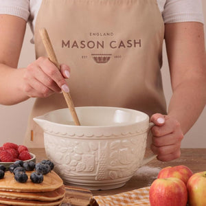 Mason Cash In the Forest Batter Bowl in cream is shown on a wooden table with someone mixing 