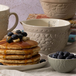 Stack of pancakes with blueberries and syrup on a plate, surrounded by ceramic Mason Cash in the forest kitchenware.