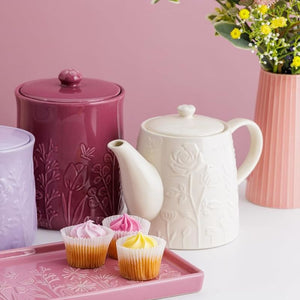 Mason Cash In The Meadow Cream Teapot next to the matching storage jar, and cupcakes on a pink platter.