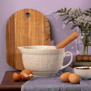 Cream Mason Cash batter bowl styled on a bench with eggs, rolling pin, and wooden board