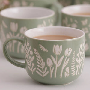 Mason Cash In The Meadow Green Tulip Mug filled with tea, with two matching blurred mugs in the background.
