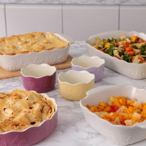 Mason Cash In The Meadow Oven Dishes filled with pies, salad, and fruit on a marble countertop with a tiled wall background.