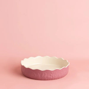 Mason Cash In The Meadow Pink Pie Dish featuring embossed floral details and a glossy white interior, set against a solid pink background.