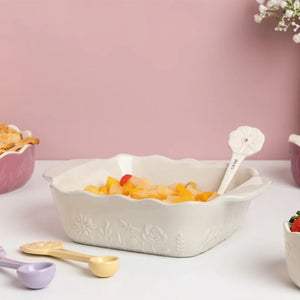 Mason Cash In The Meadow Square Oven Dish filled with fruit pieces and a white spoon, set on a white table against a pink background with other pastel-colored bowls and spoons nearby.