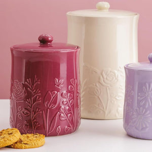 Three Mason Cash In The Meadow Storage Jars with floral embossing on a pink background