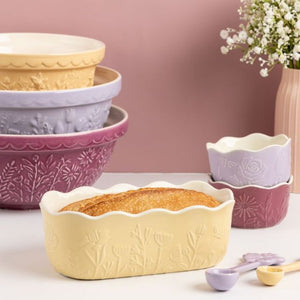 Mason Cash In The Meadow Yellow Loaf Pan styled next to coordinating ceramic bowls on a pink background.