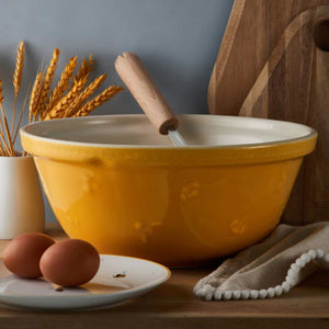 Mason Cash Sweet Bee Yellow Mixing Bowl styled with eggs, whisk and wheat stalks on rustic table.